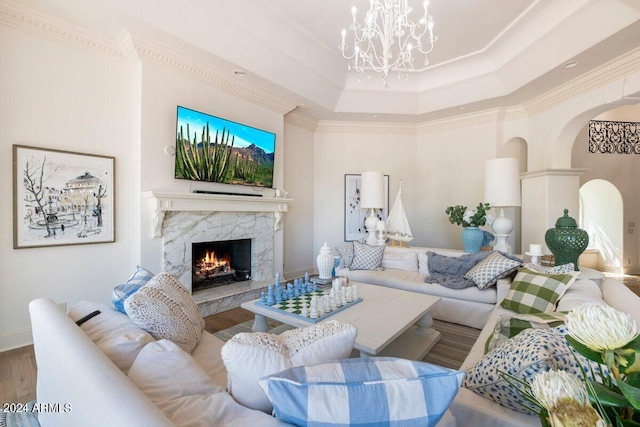 living room with wood-type flooring, a fireplace, an inviting chandelier, a raised ceiling, and crown molding