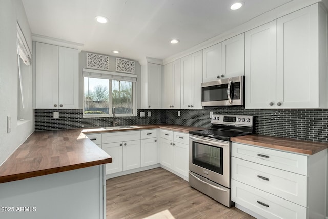 kitchen with butcher block counters, white cabinetry, sink, backsplash, and stainless steel appliances