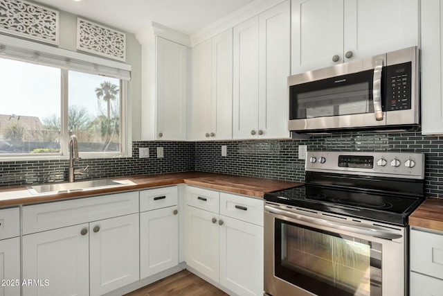 kitchen with butcher block counters, tasteful backsplash, sink, white cabinets, and stainless steel appliances