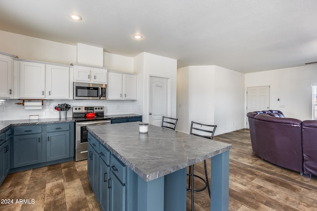 kitchen featuring dark wood-type flooring, stainless steel appliances, a center island, white cabinets, and tasteful backsplash