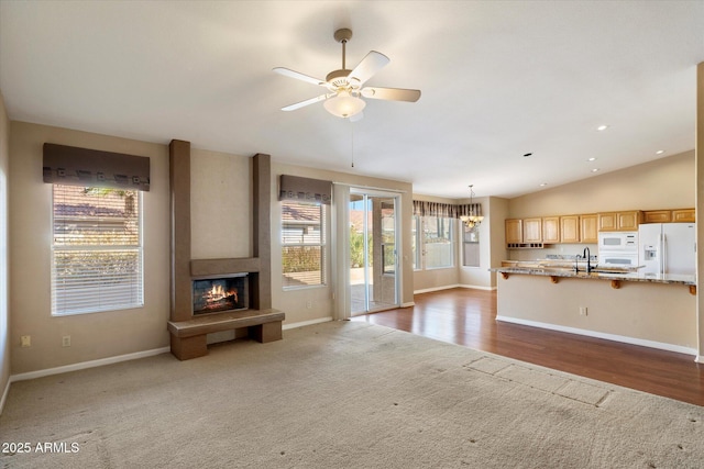 unfurnished living room featuring sink, dark colored carpet, a large fireplace, ceiling fan with notable chandelier, and vaulted ceiling