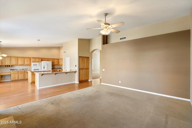 unfurnished living room with sink, ceiling fan with notable chandelier, light colored carpet, and high vaulted ceiling