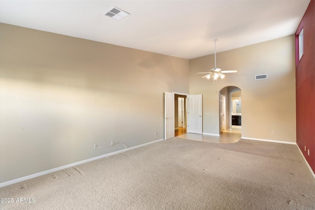 carpeted spare room featuring a towering ceiling and ceiling fan