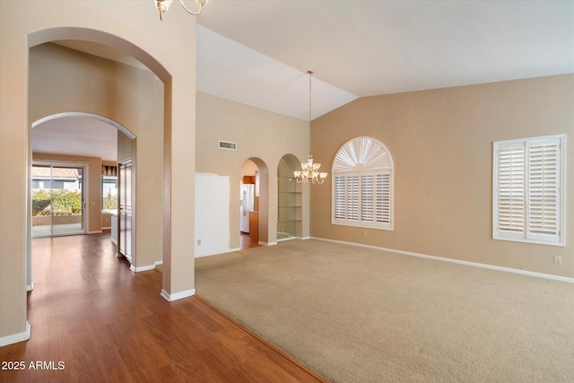 carpeted empty room with high vaulted ceiling and an inviting chandelier