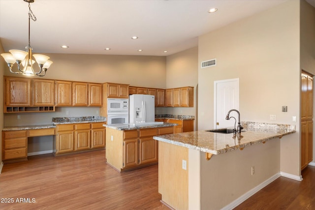 kitchen featuring sink, decorative light fixtures, kitchen peninsula, white appliances, and light stone countertops