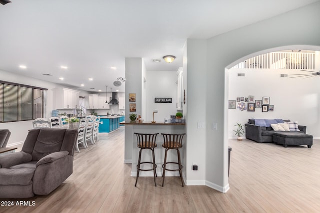 kitchen with white cabinets, wall chimney exhaust hood, light wood-type flooring, a kitchen bar, and kitchen peninsula