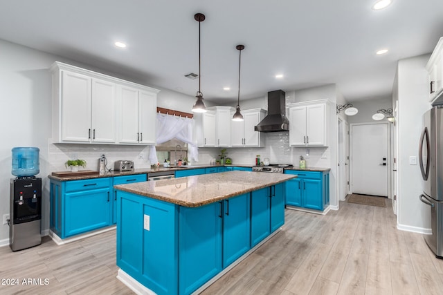 kitchen featuring wall chimney exhaust hood, stainless steel appliances, blue cabinetry, decorative light fixtures, and a center island