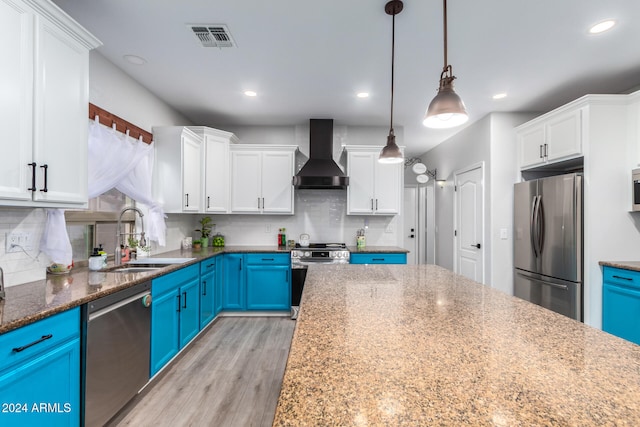 kitchen with sink, stainless steel appliances, wall chimney range hood, blue cabinets, and pendant lighting