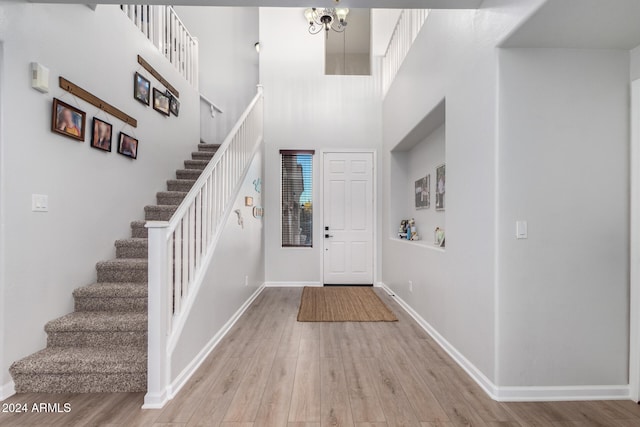 foyer entrance featuring a towering ceiling, light hardwood / wood-style flooring, and a notable chandelier