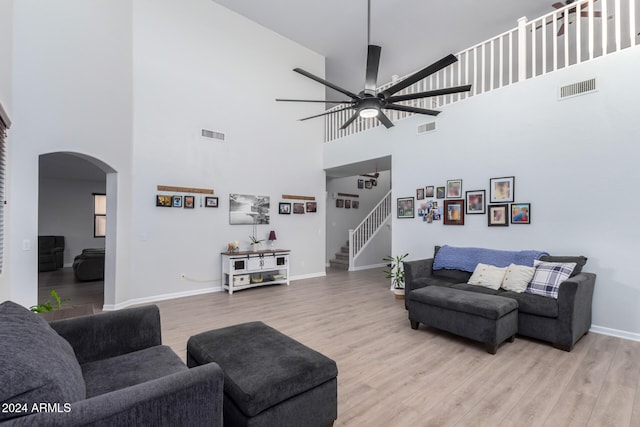 living room with ceiling fan, light hardwood / wood-style flooring, and a towering ceiling