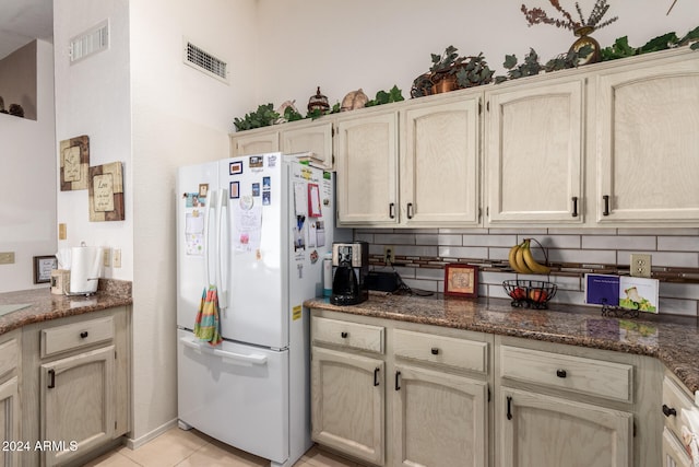 kitchen with tasteful backsplash, light tile patterned flooring, dark stone counters, and white refrigerator