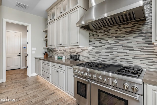 kitchen with white cabinetry, light hardwood / wood-style flooring, wall chimney range hood, range with two ovens, and backsplash