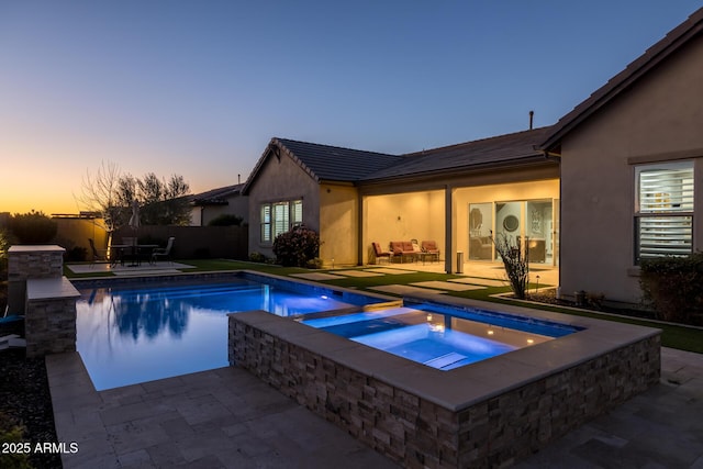 pool at dusk with an in ground hot tub and a patio area