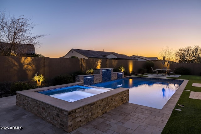 pool at dusk with an in ground hot tub and a patio