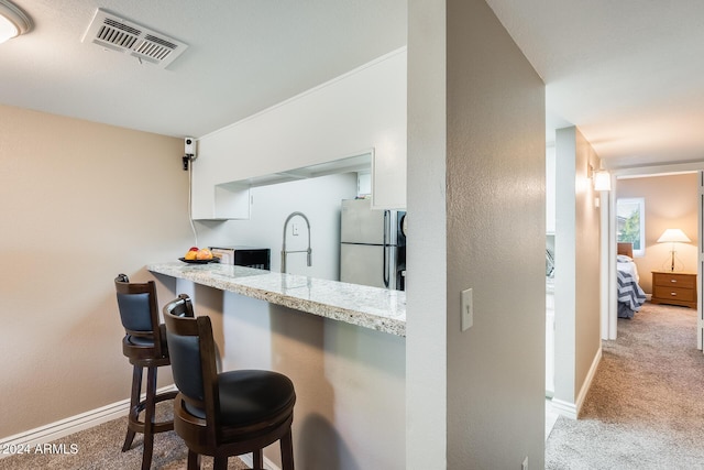 kitchen with a kitchen breakfast bar, light colored carpet, stainless steel refrigerator, and white cabinetry