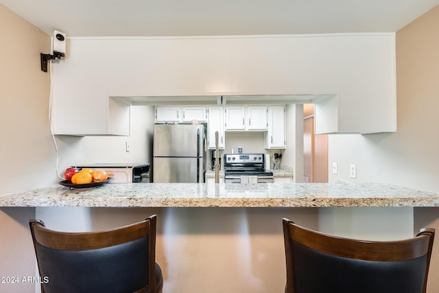 kitchen featuring a kitchen bar, appliances with stainless steel finishes, white cabinets, and kitchen peninsula