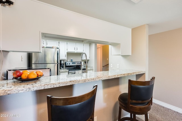 kitchen featuring carpet flooring, appliances with stainless steel finishes, kitchen peninsula, a breakfast bar, and white cabinetry