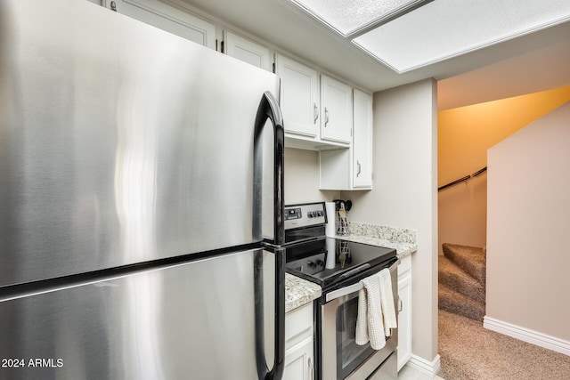 kitchen with white cabinets, appliances with stainless steel finishes, light colored carpet, and light stone counters