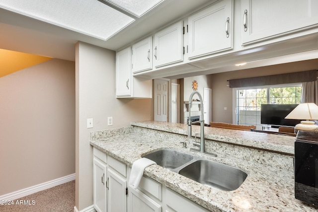 kitchen featuring carpet flooring, light stone counters, white cabinetry, and sink