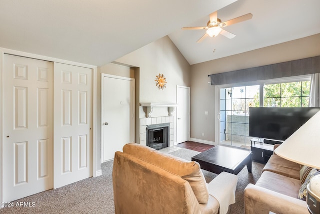 living room with a tiled fireplace, ceiling fan, carpet floors, and vaulted ceiling