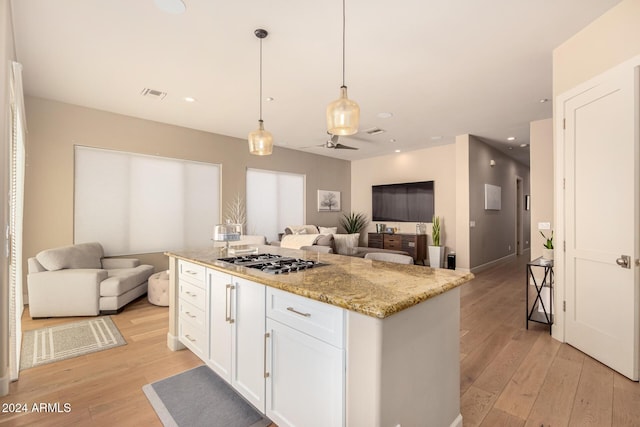 kitchen featuring stainless steel gas stovetop, decorative light fixtures, a center island, and white cabinetry