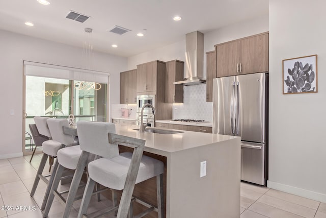 kitchen with stainless steel appliances, a breakfast bar, wall chimney exhaust hood, light tile patterned flooring, and a center island with sink