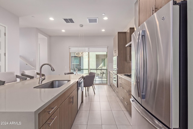 kitchen featuring an island with sink, stainless steel appliances, sink, decorative light fixtures, and light tile patterned floors