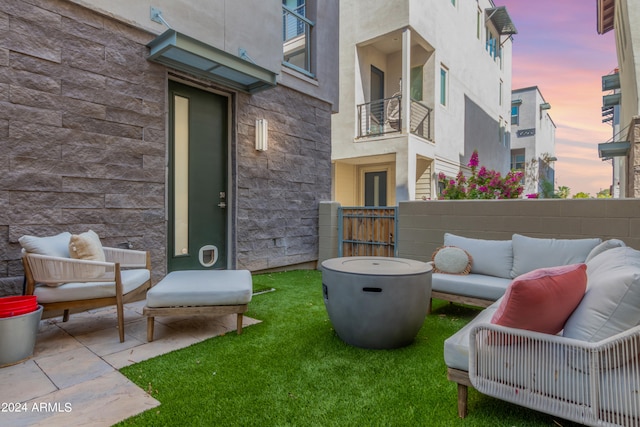 patio terrace at dusk featuring outdoor lounge area, a balcony, and a lawn