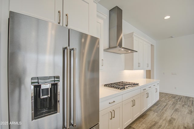 kitchen with stainless steel appliances, light countertops, light wood-type flooring, wall chimney range hood, and backsplash