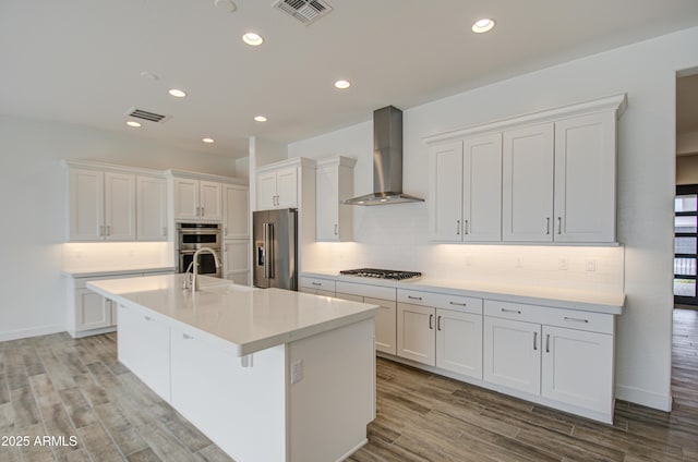 kitchen featuring visible vents, white cabinets, appliances with stainless steel finishes, wall chimney exhaust hood, and tasteful backsplash