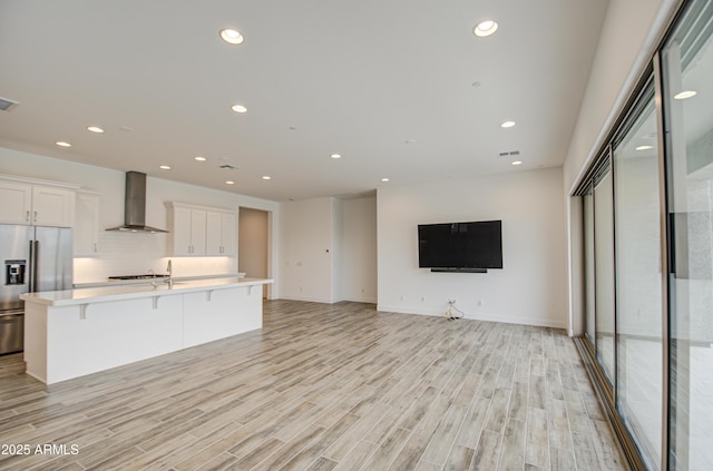 kitchen with recessed lighting, white cabinetry, light countertops, wall chimney range hood, and stainless steel fridge with ice dispenser