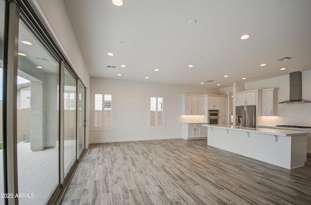 kitchen featuring stainless steel appliances, visible vents, white cabinetry, light wood-type flooring, and wall chimney exhaust hood