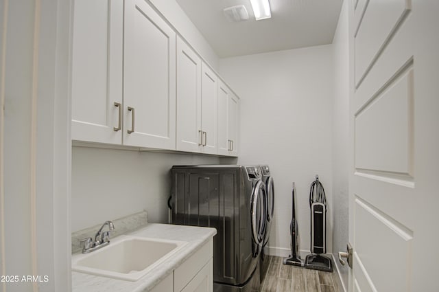 washroom with wood finished floors, a sink, baseboards, cabinet space, and washing machine and clothes dryer