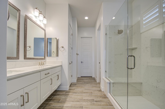 bathroom featuring double vanity, wood finish floors, a shower stall, a sink, and recessed lighting