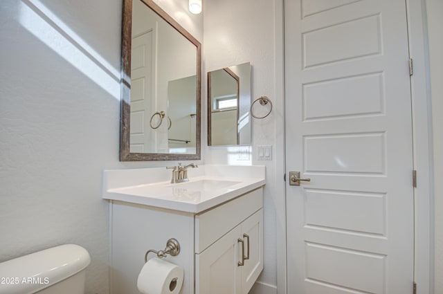 bathroom with a textured wall, vanity, and toilet