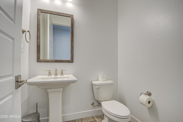 bathroom with toilet, a sink, baseboards, and wood finished floors