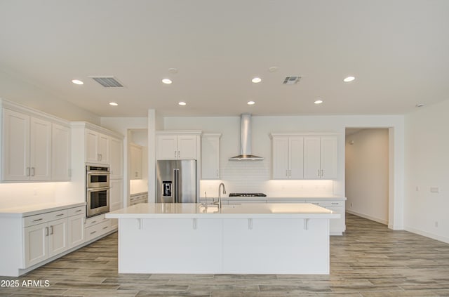 kitchen with stainless steel appliances, visible vents, a sink, and wall chimney exhaust hood