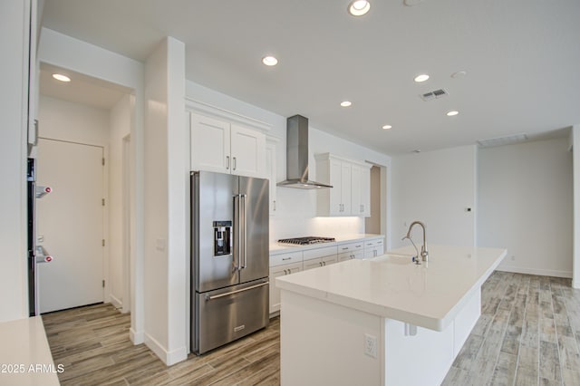 kitchen with light wood-style flooring, gas stovetop, visible vents, high end fridge, and wall chimney range hood