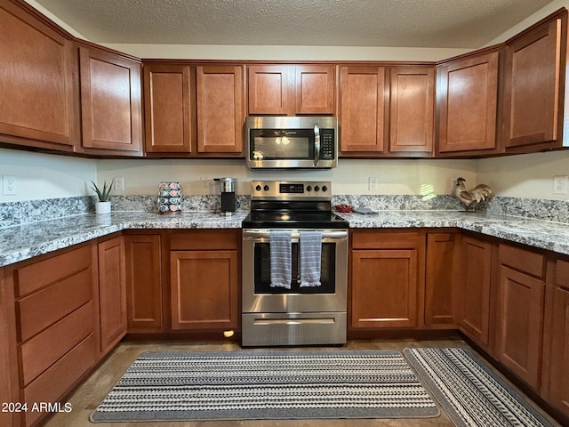 kitchen with stainless steel appliances, light stone countertops, and a textured ceiling