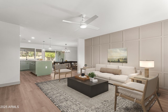 living room featuring ceiling fan with notable chandelier and light wood-type flooring