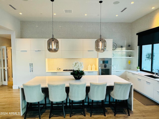 kitchen with pendant lighting, a kitchen island, stainless steel double oven, and light wood-type flooring