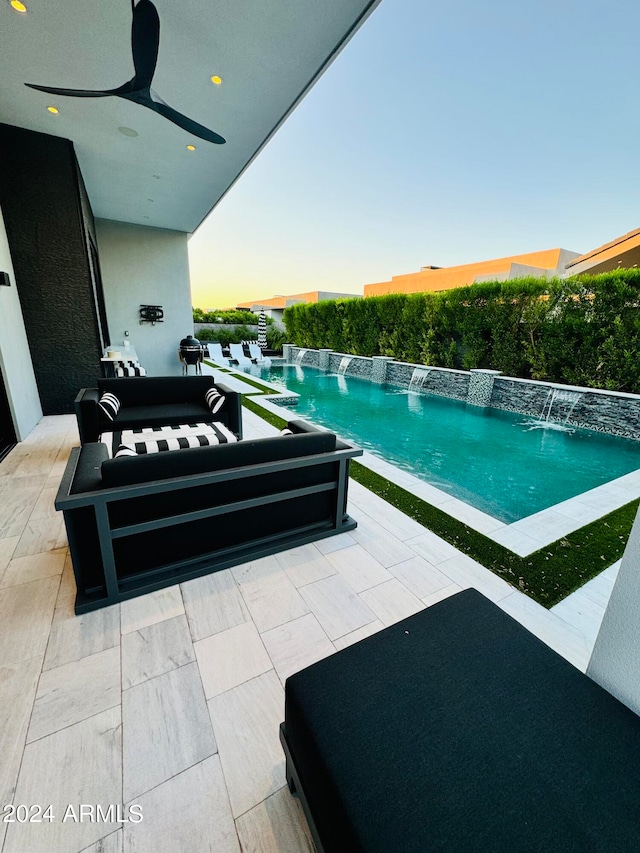 pool at dusk with a patio area, pool water feature, and ceiling fan