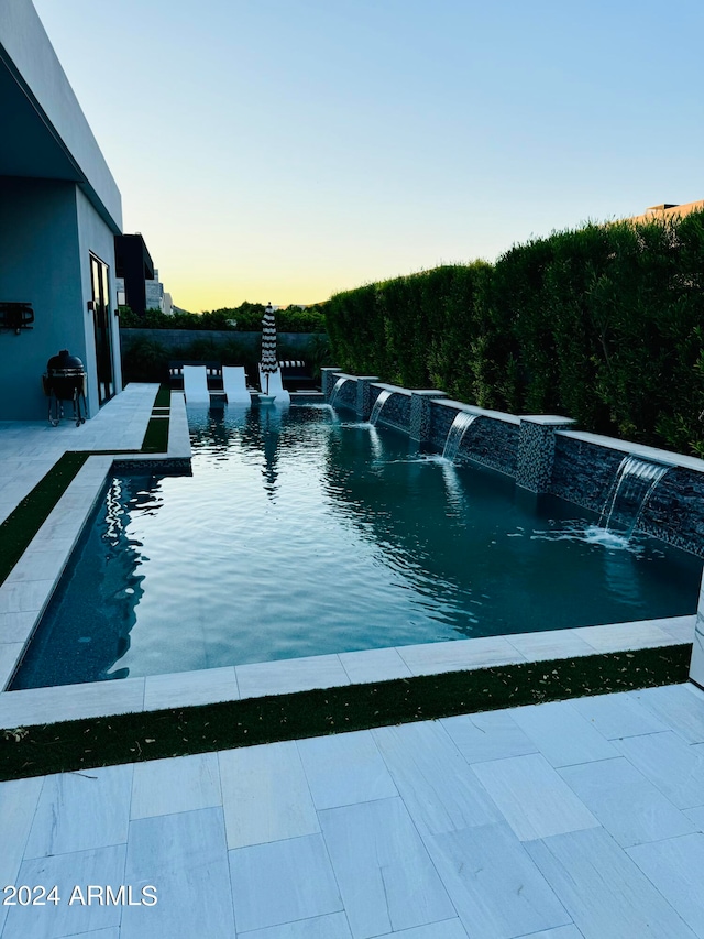 pool at dusk featuring pool water feature and grilling area