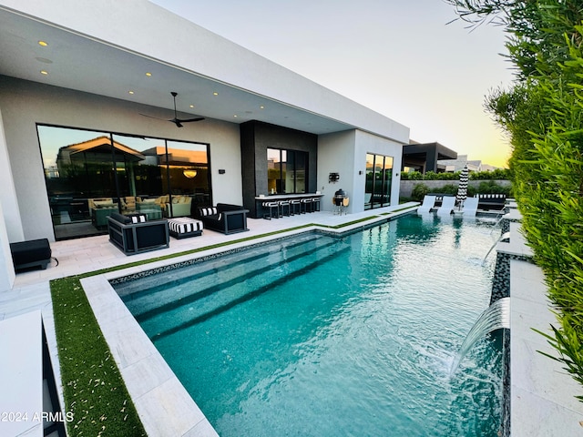 pool at dusk featuring ceiling fan and a patio