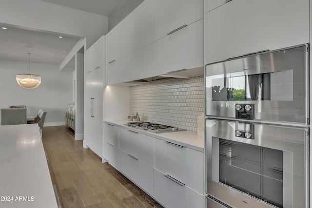 kitchen with appliances with stainless steel finishes, tasteful backsplash, hanging light fixtures, light wood-type flooring, and white cabinets