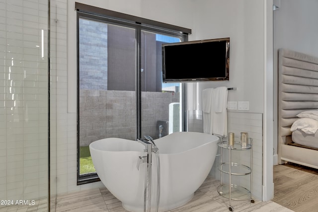 bathroom featuring tile walls, hardwood / wood-style floors, a washtub, and plenty of natural light