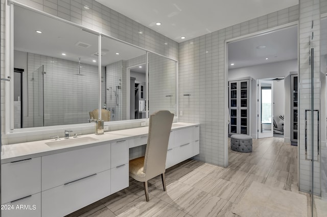 bathroom with a shower with door, vanity, and tile walls