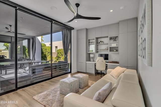 living room with built in desk, ceiling fan, light wood-type flooring, and floor to ceiling windows