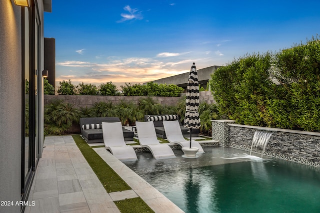 pool at dusk with pool water feature and a patio