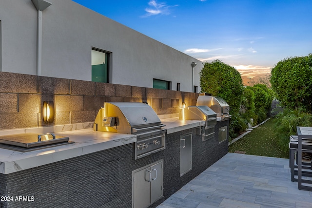 patio terrace at dusk featuring area for grilling and a grill